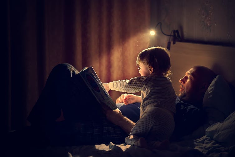 Un homme et un enfant lisent un livre, assis sur un lit