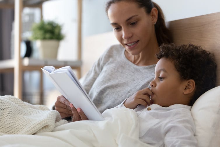 Une femme lit un livre à un enfant, assis sur un lit